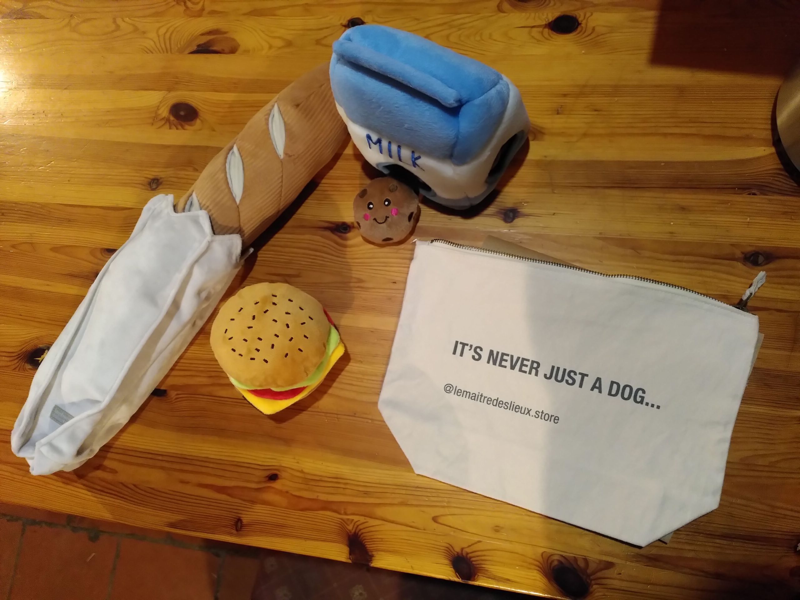 Des jouets pour chien en forme d'aliment. Il y a une baguette, un hamburger, une brique de lait et des cookies.
