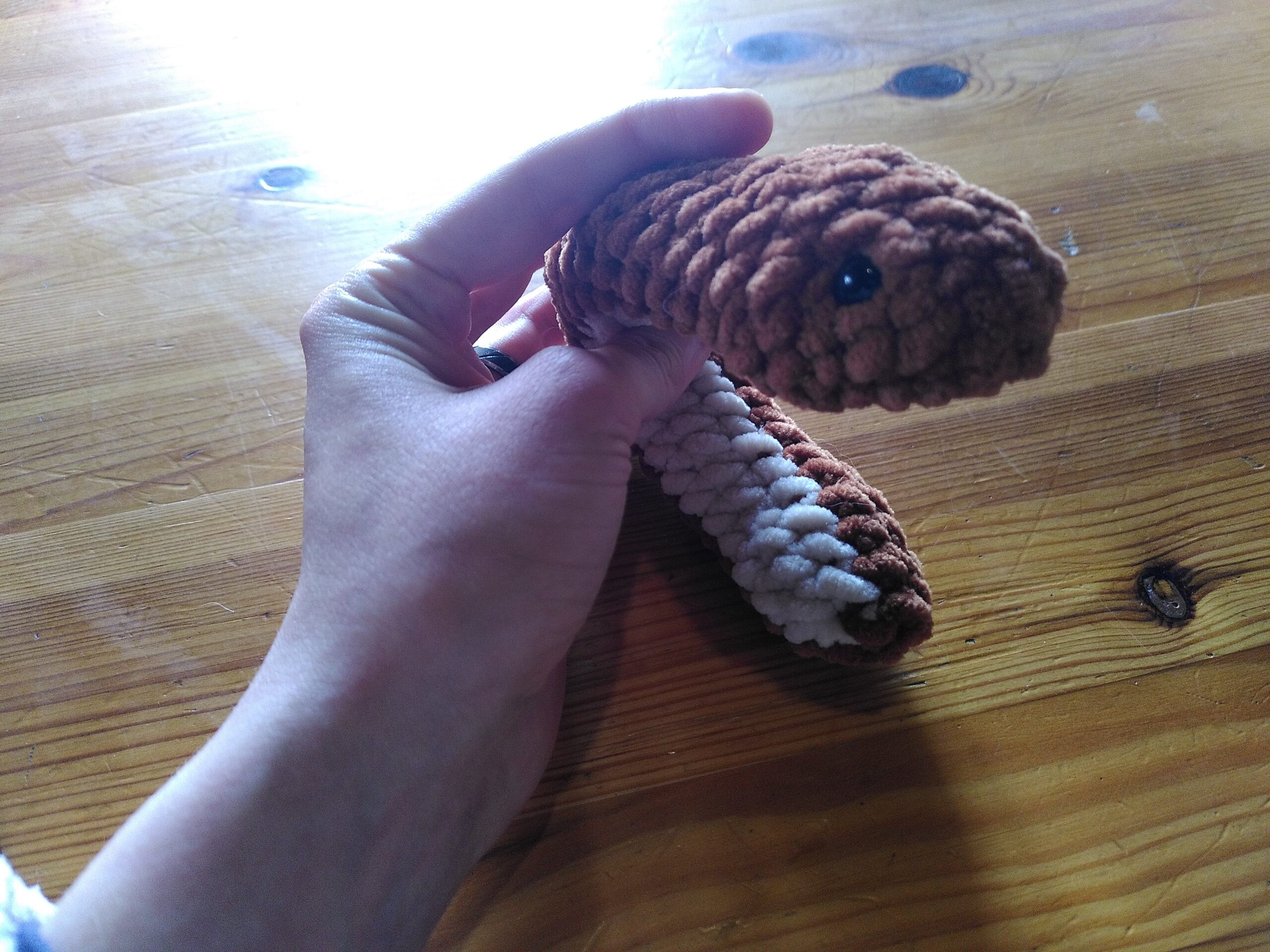 Un serpent en crochet, son corps est marron et son ventre est beige. Il est courbé de manière à voir sa tête de dessus et son ventre.